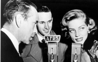 Black and white picture from the first half of the 20th century showing two men and a woman talking into microphones