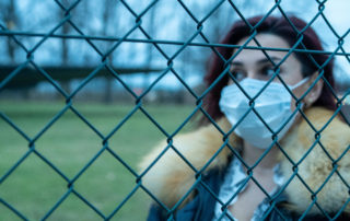 Woman behind a metal fence with a mask over her nose and mouth