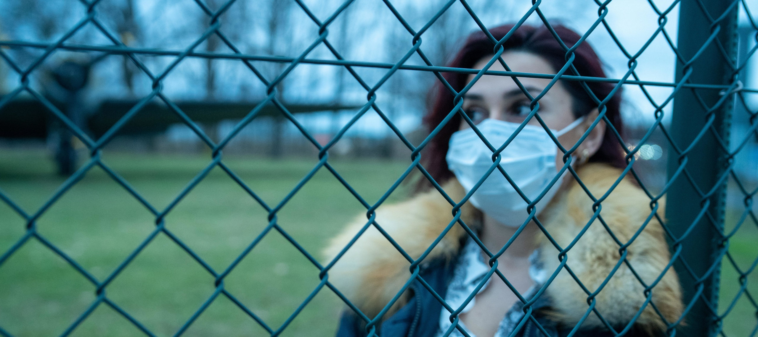 Woman behind a metal fence with a mask over her nose and mouth