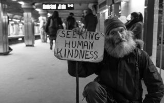 Homeless man with a sign that says "Seeking human kindness"