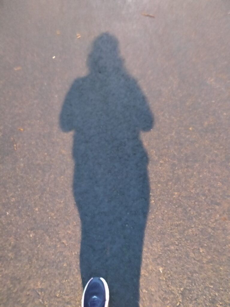 The shadow of a woman walking on a road with the tip of one running shoe