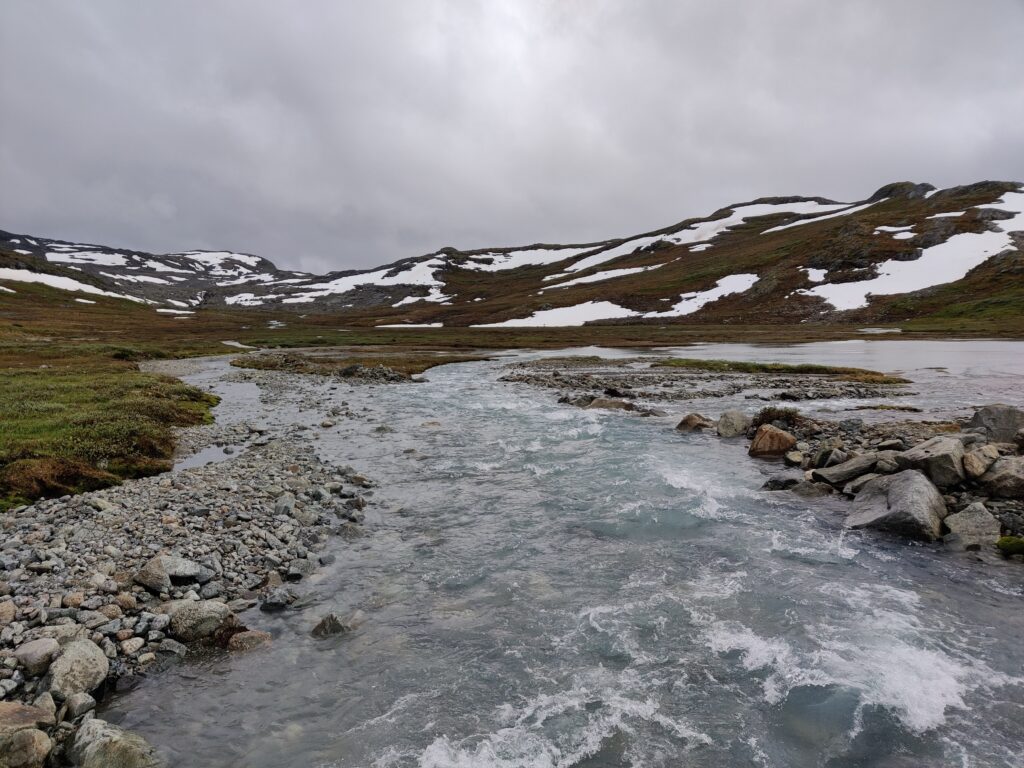 View from a bridge over glacial melit water running down from the mountains in Norway; stormy sky