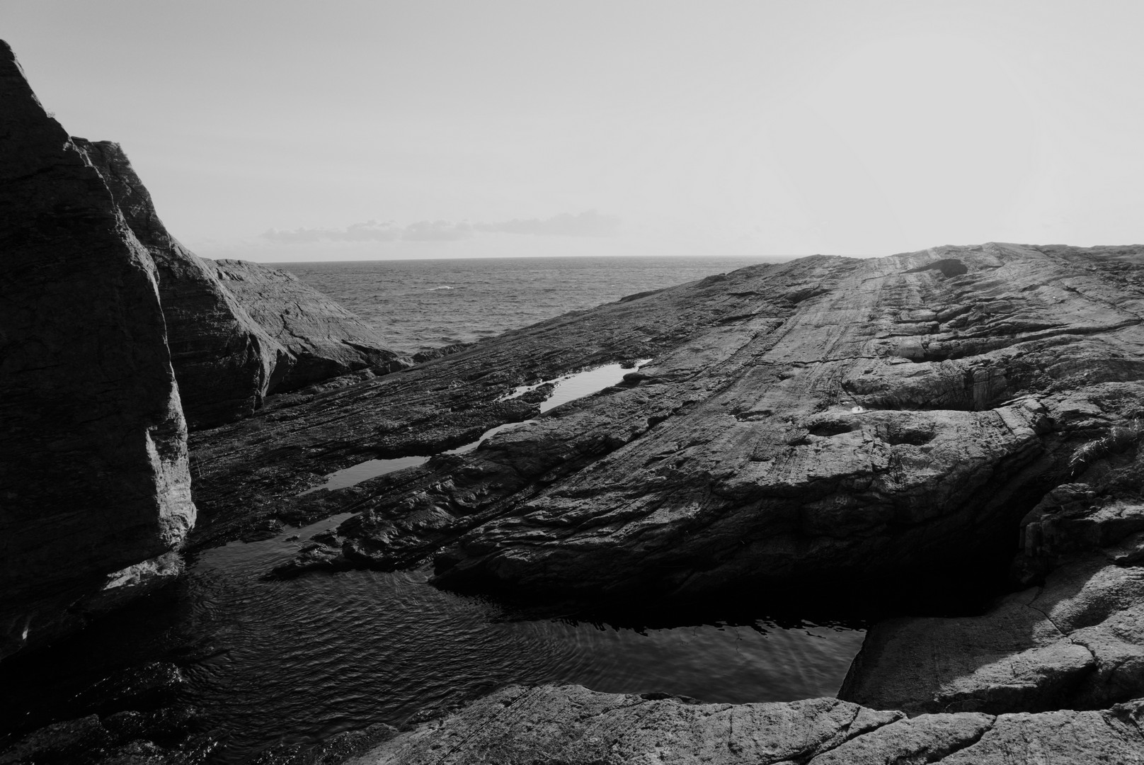 Black and white picture taken where land meets the sea. Rocky surface that looks like a runway and behind it the sea on the horizon.