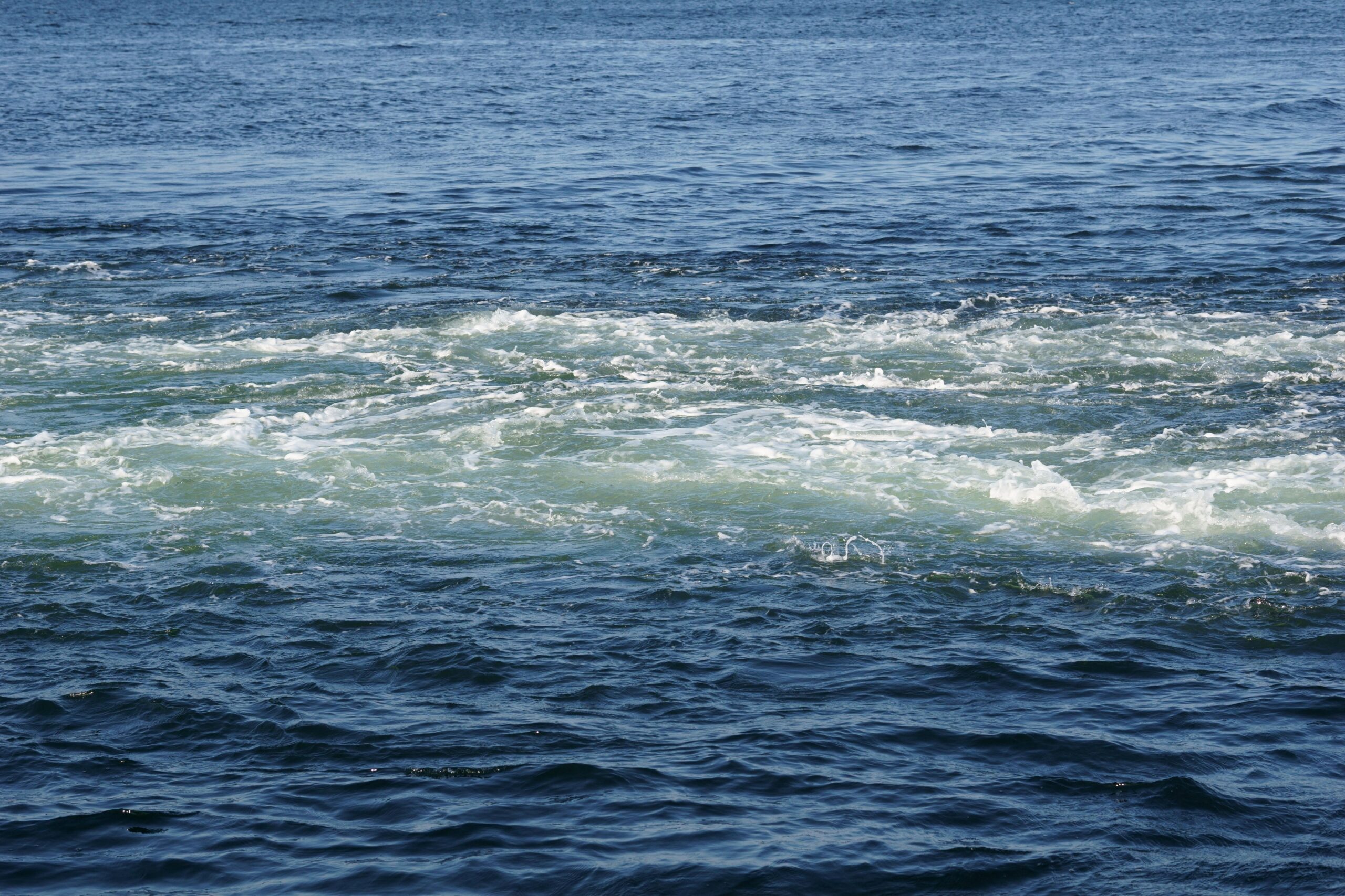 Rough, shoppy waters. Dark blue water and lighter blue water where a boat has passed and cut through the water,